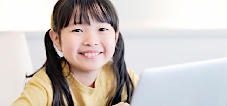 ノートパソコンの前で笑顔になっている子供の写真