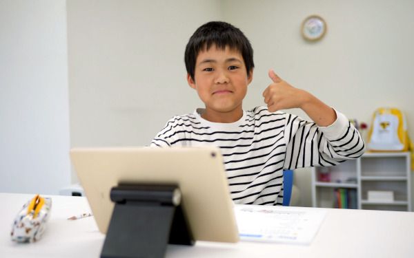 タブレットの前で親指を立てて微笑んでいる男の子