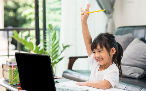 ノートパソコンの向こうにいるチューターに手を挙げてアピールをする女の子